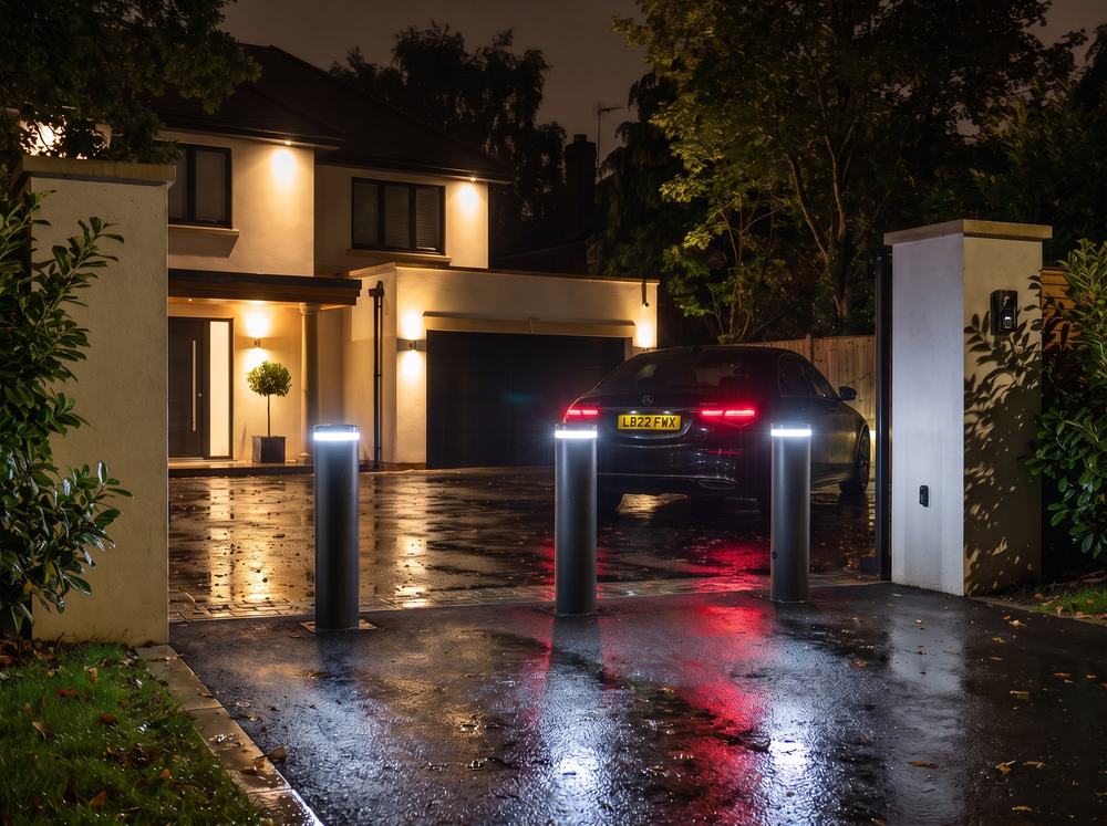 Three automatic bollards with glowing LED tops raised across a driveway entrance at night