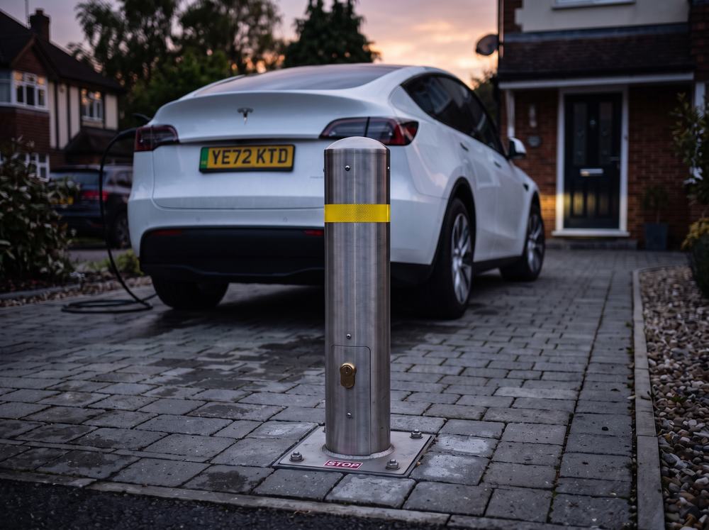 A raised telescopic bollard behind a white Tesla parked on a block-paved driveway
